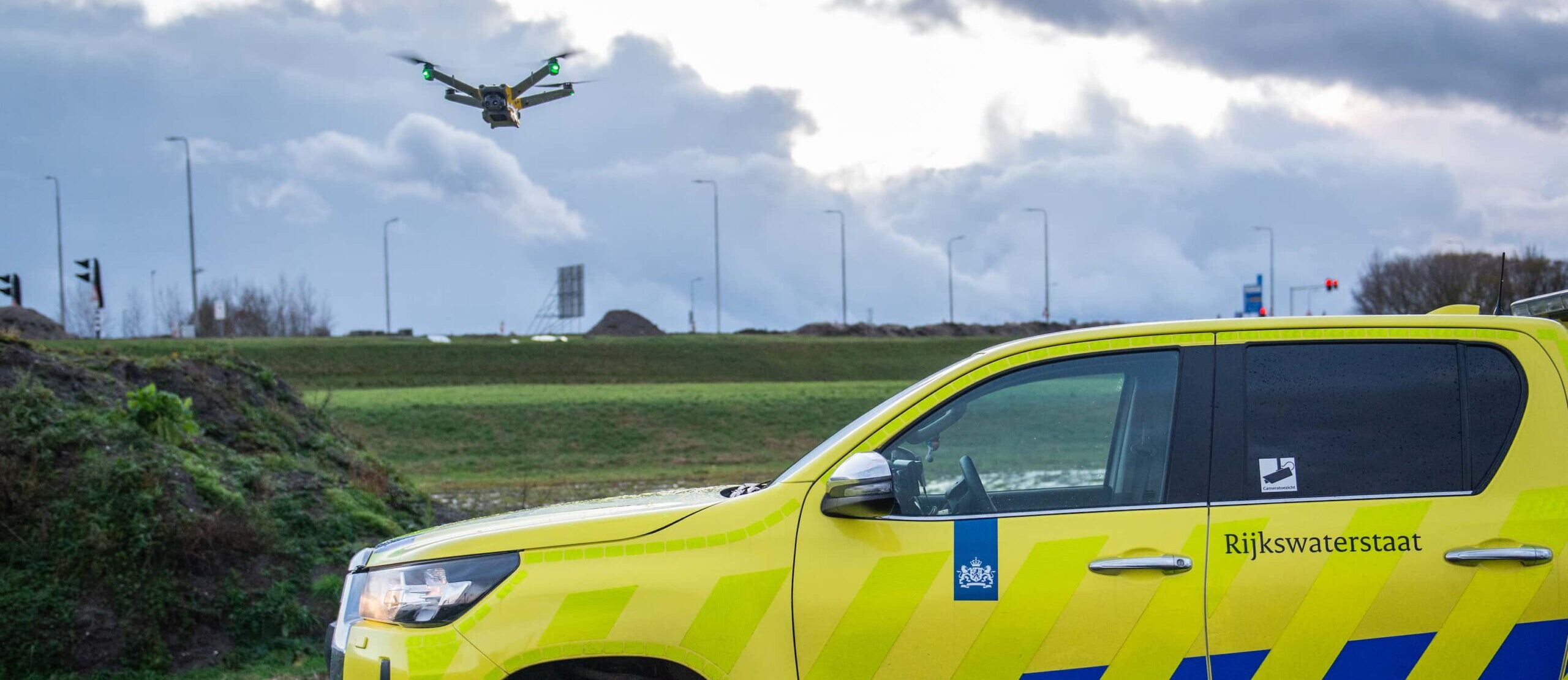 Een drone vliegt bij een auto van een weginspecteur van Rijkswaterstaat.